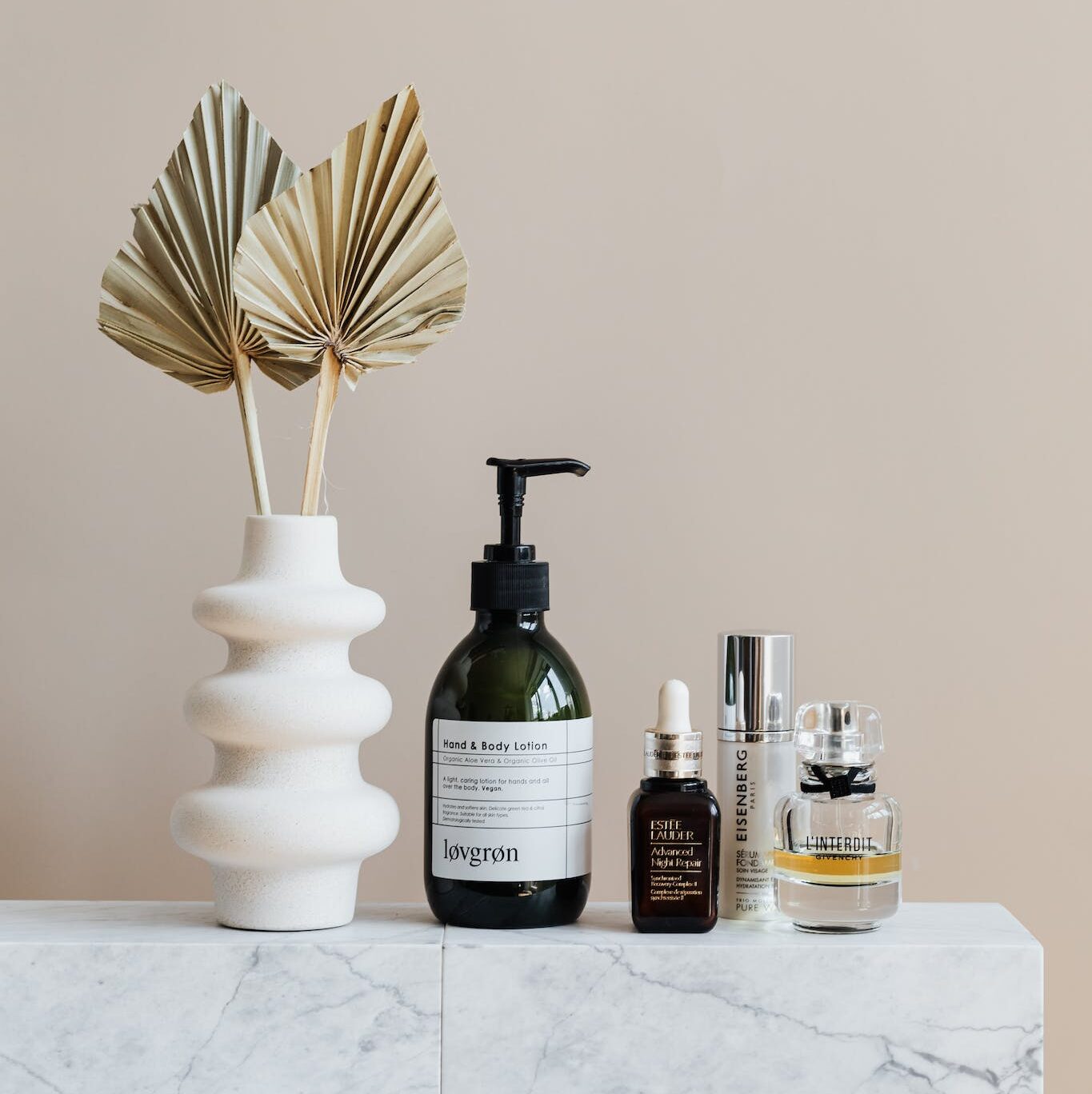 Set of cosmetic supplies near decorative leaves in vase on marble shelf